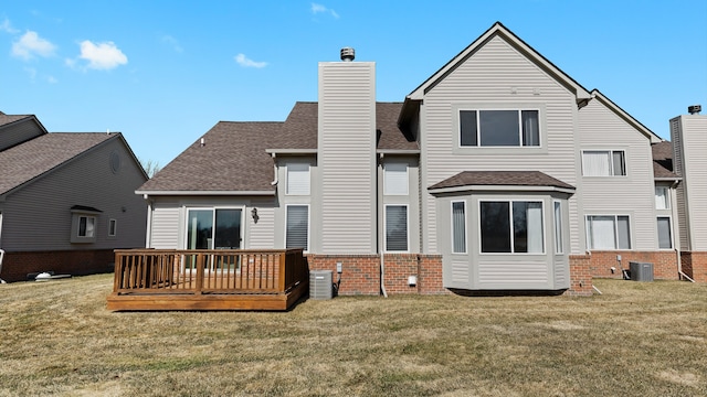 back of property featuring a shingled roof, a deck, central air condition unit, a lawn, and brick siding