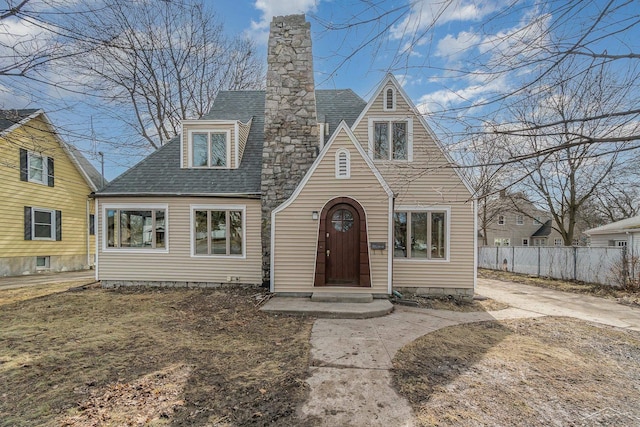 view of front facade with fence, roof with shingles, and a chimney