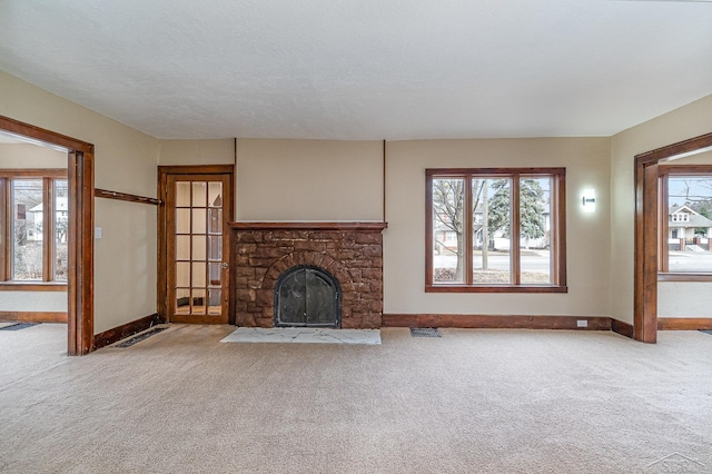 unfurnished living room with a stone fireplace, baseboards, visible vents, and carpet floors