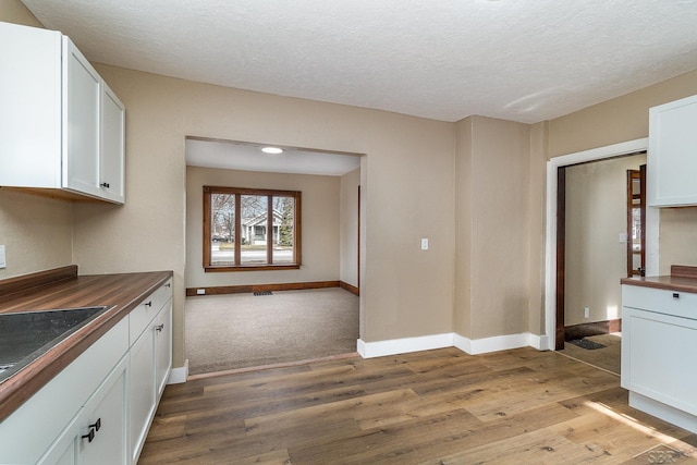 kitchen with white cabinets, a textured ceiling, baseboards, and light wood-style floors