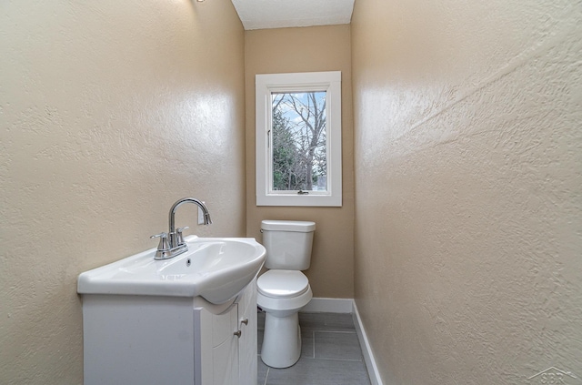 bathroom with tile patterned floors, toilet, baseboards, vanity, and a textured wall