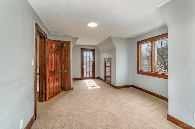 spare room with light colored carpet, a textured ceiling, baseboards, and a textured wall