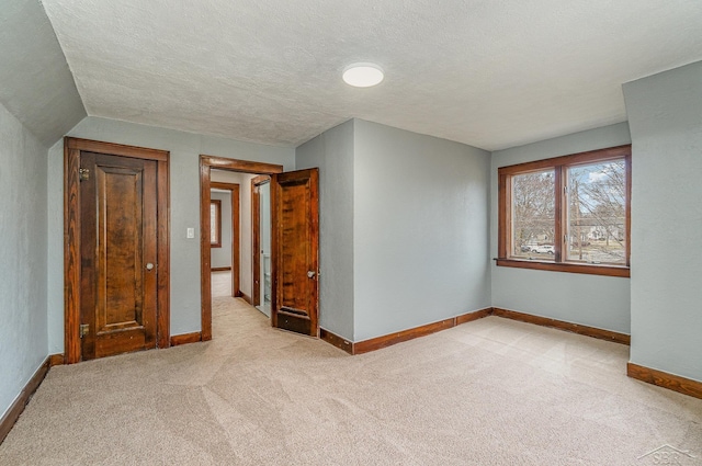 empty room with light carpet, a textured ceiling, and baseboards