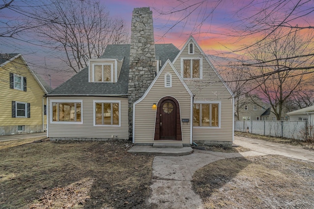 view of front facade featuring a shingled roof, a chimney, and fence