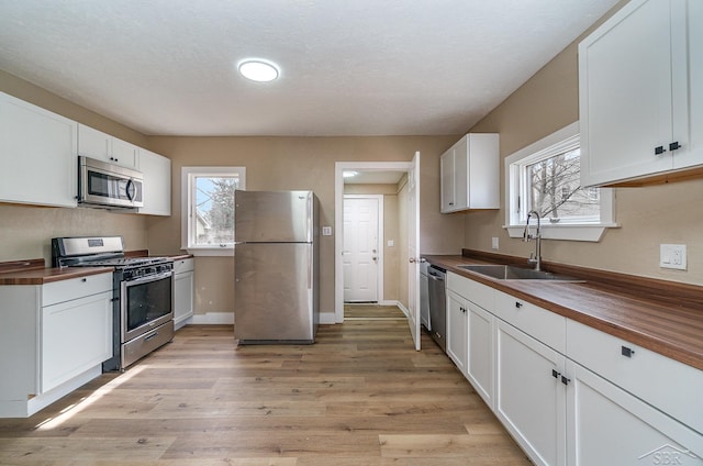 kitchen with a sink, butcher block countertops, light wood-type flooring, and stainless steel appliances