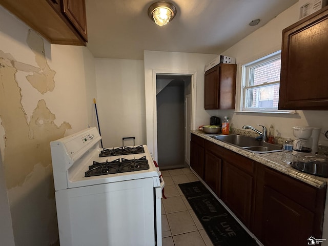 kitchen featuring a sink, dark brown cabinetry, light countertops, light tile patterned floors, and white range with gas stovetop