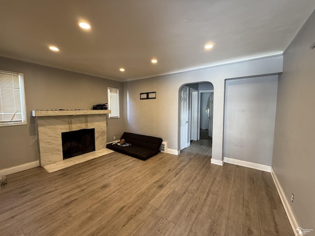 unfurnished living room with a tiled fireplace, wood finished floors, recessed lighting, arched walkways, and baseboards