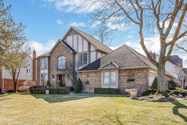 tudor-style house featuring brick siding, a front lawn, roof with shingles, a chimney, and an attached garage