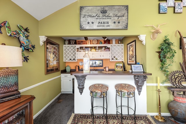 kitchen featuring dark countertops, lofted ceiling, a kitchen breakfast bar, a peninsula, and dark colored carpet