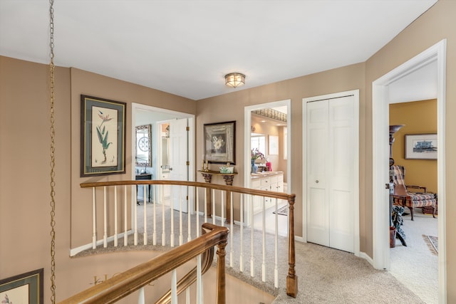 hallway featuring light carpet, an upstairs landing, and baseboards