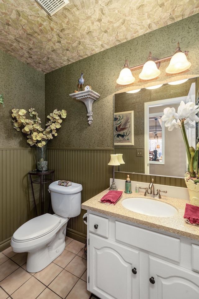 bathroom with visible vents, a wainscoted wall, wallpapered walls, tile patterned floors, and toilet