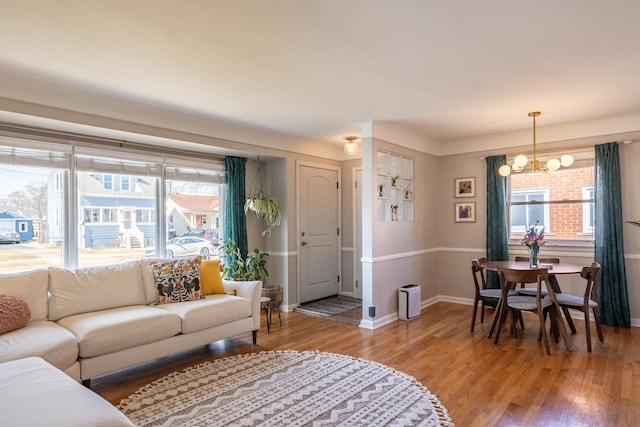 living room featuring an inviting chandelier, baseboards, and light wood-type flooring