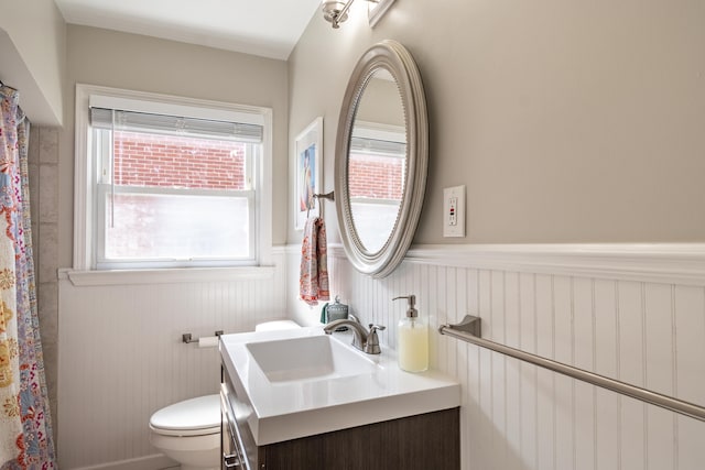 full bath featuring curtained shower, vanity, toilet, and wainscoting