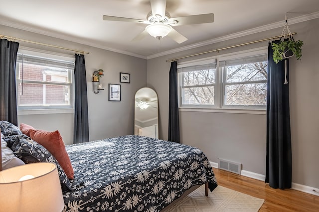 bedroom featuring wood finished floors, baseboards, visible vents, ceiling fan, and ornamental molding