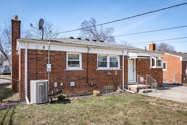 rear view of house with brick siding, a chimney, central AC, and fence