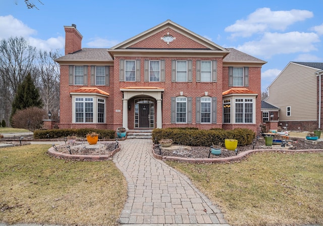 view of front of home featuring a front lawn, brick siding, and a chimney