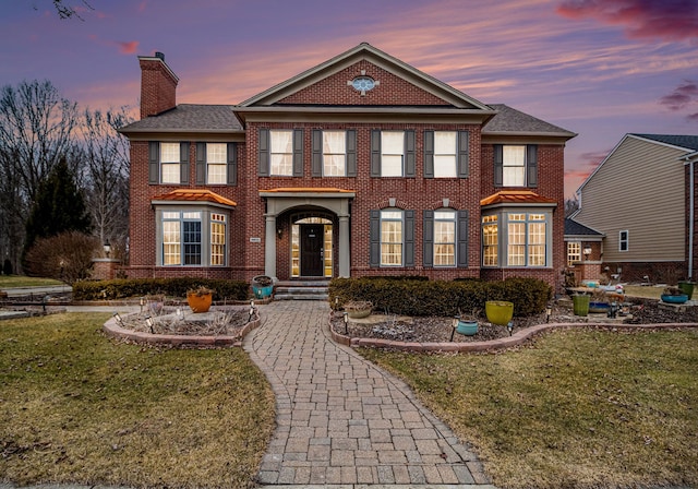 colonial home featuring a lawn, brick siding, and a chimney