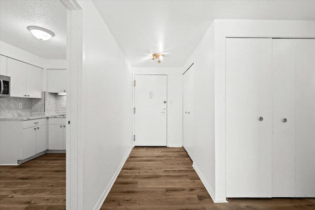 corridor with wood finished floors, baseboards, and a textured ceiling