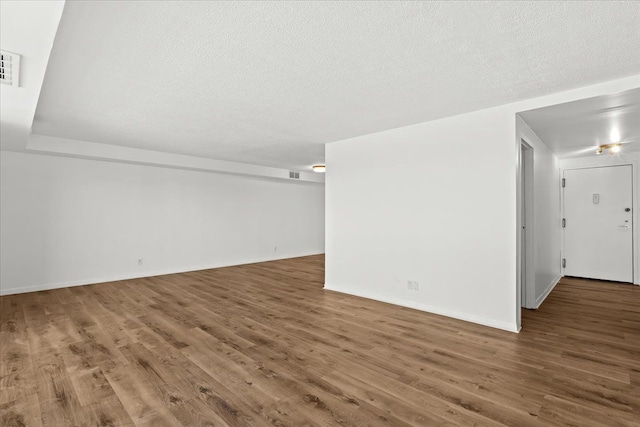 empty room featuring visible vents, a textured ceiling, baseboards, and wood finished floors