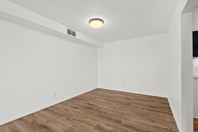 empty room featuring baseboards, wood finished floors, visible vents, and a textured ceiling