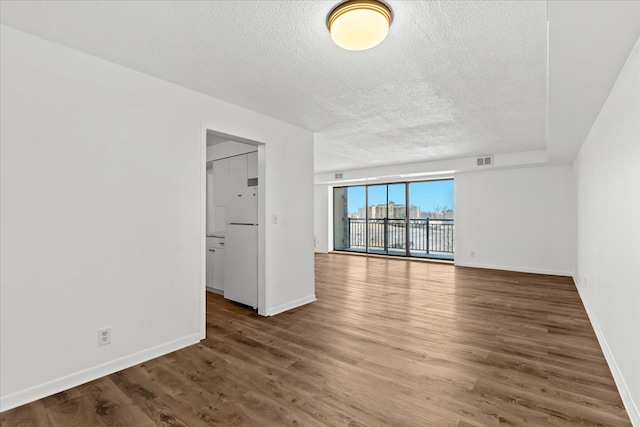 unfurnished room featuring baseboards, wood finished floors, visible vents, and a textured ceiling