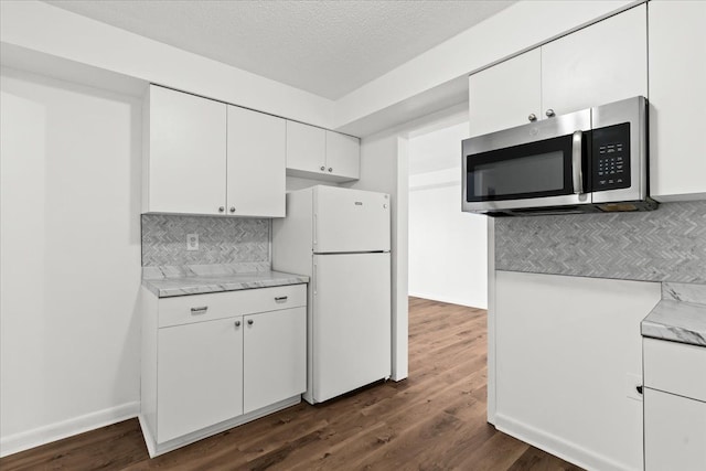 kitchen featuring dark wood-style flooring, freestanding refrigerator, white cabinets, stainless steel microwave, and backsplash