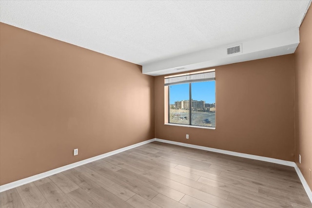 spare room with visible vents, baseboards, light wood finished floors, a textured ceiling, and a view of city