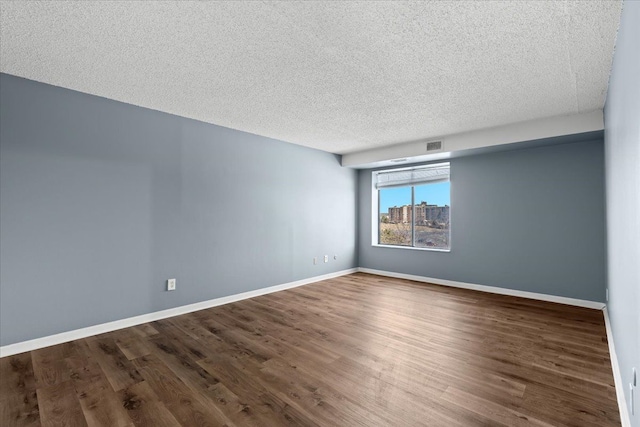 unfurnished room with visible vents, baseboards, a textured ceiling, and wood finished floors