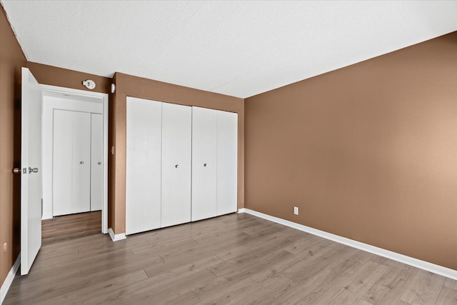 unfurnished bedroom featuring a closet, a textured ceiling, baseboards, and wood finished floors