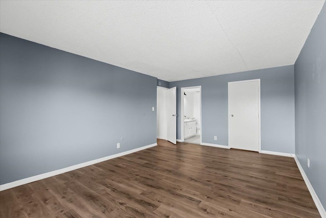 unfurnished bedroom featuring a textured ceiling, ensuite bath, baseboards, and wood finished floors