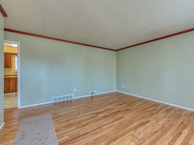 empty room featuring light wood finished floors, visible vents, crown molding, and baseboards