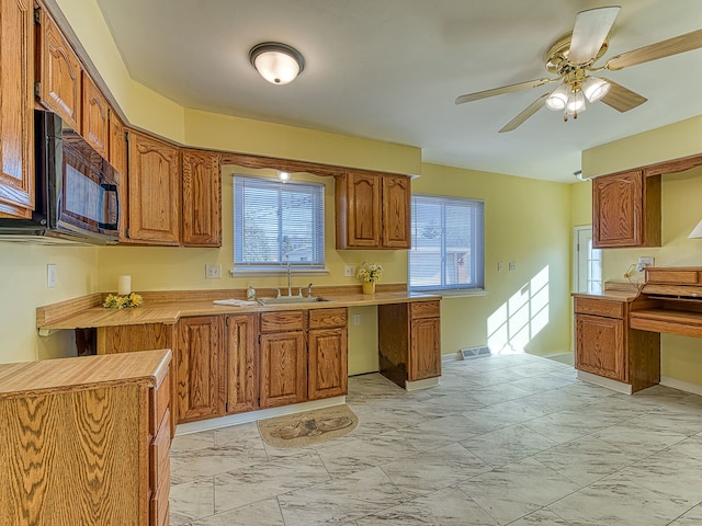 kitchen with light countertops, brown cabinetry, marble finish floor, and black microwave