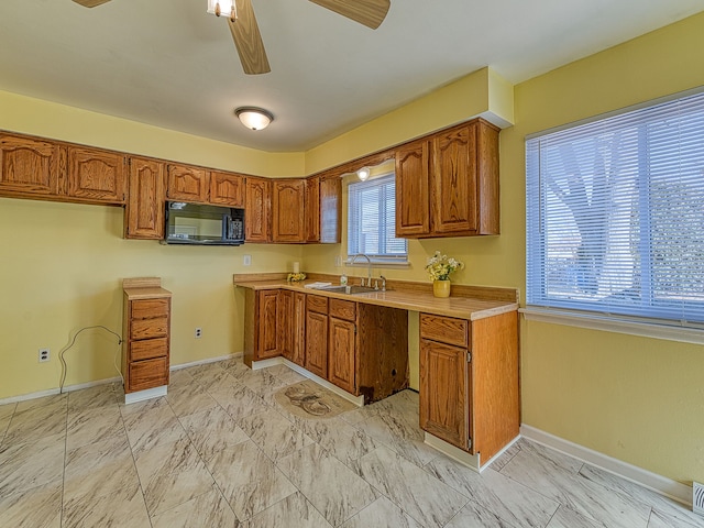 kitchen with brown cabinets, marble finish floor, a sink, black microwave, and light countertops