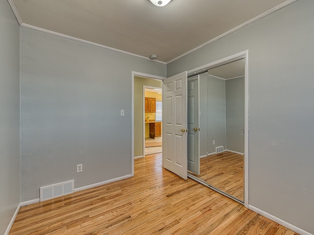 empty room featuring baseboards, visible vents, ornamental molding, a barn door, and light wood-type flooring