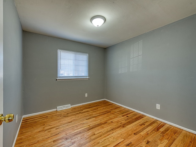 unfurnished room featuring a textured ceiling, wood finished floors, visible vents, and baseboards