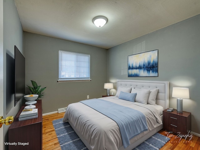 bedroom with visible vents, a textured ceiling, baseboards, and wood finished floors