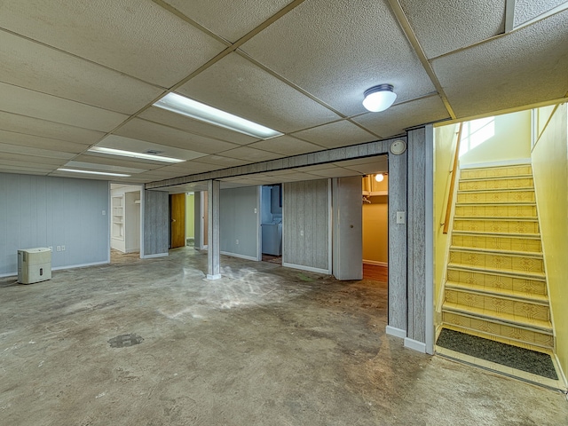 finished below grade area with stairway, a paneled ceiling, and baseboards