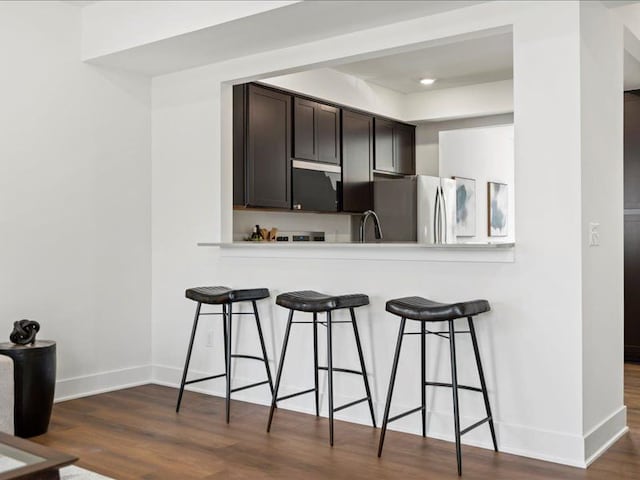 kitchen with a kitchen breakfast bar, dark wood-style floors, baseboards, and freestanding refrigerator