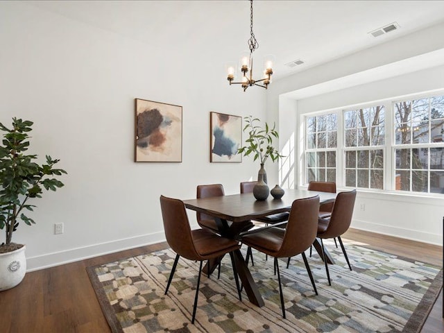 dining area with a notable chandelier, visible vents, baseboards, and wood finished floors