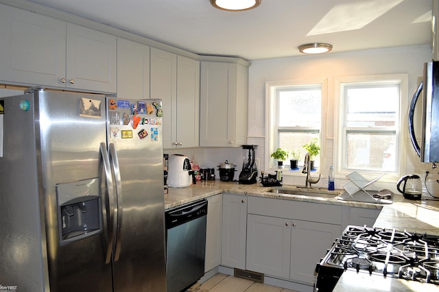 kitchen with tasteful backsplash, appliances with stainless steel finishes, light stone counters, and a sink