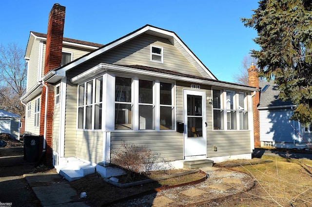 bungalow with entry steps, a sunroom, and a chimney