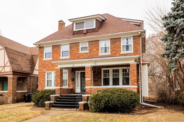 traditional style home featuring brick siding, roof with shingles, covered porch, and a chimney