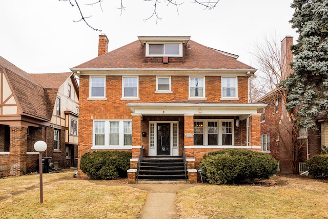 american foursquare style home featuring a front yard, brick siding, roof with shingles, and a chimney