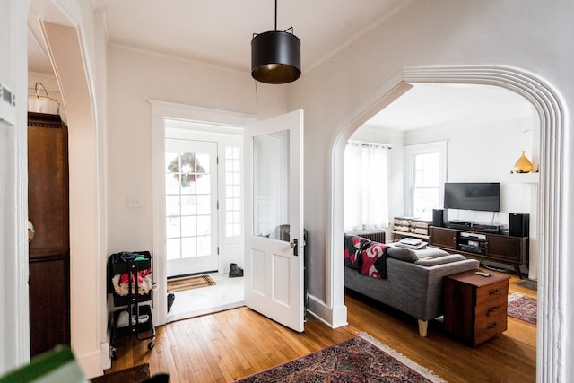 entrance foyer with arched walkways, crown molding, and hardwood / wood-style flooring