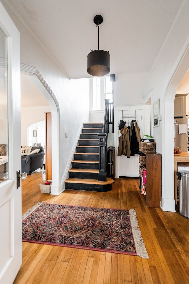 stairs with arched walkways, ornamental molding, baseboards, and hardwood / wood-style floors