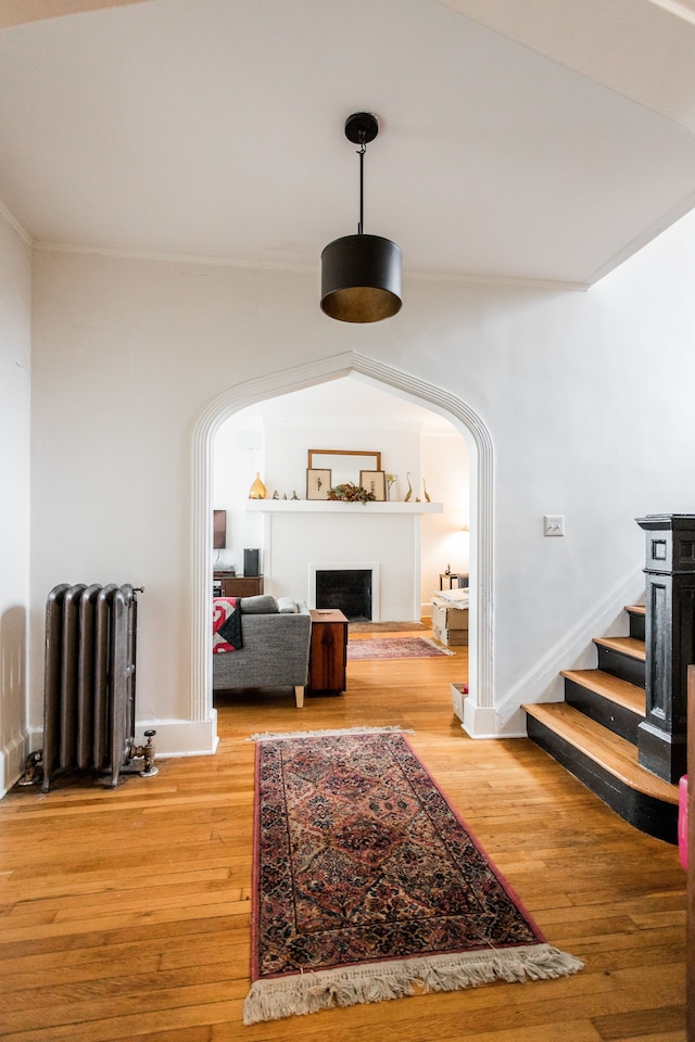 corridor with stairway, radiator, arched walkways, and light wood-type flooring