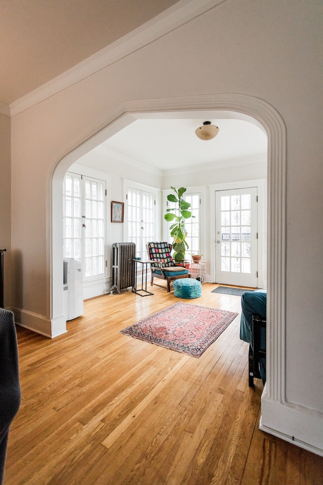 living area featuring wood finished floors, arched walkways, plenty of natural light, and ornamental molding