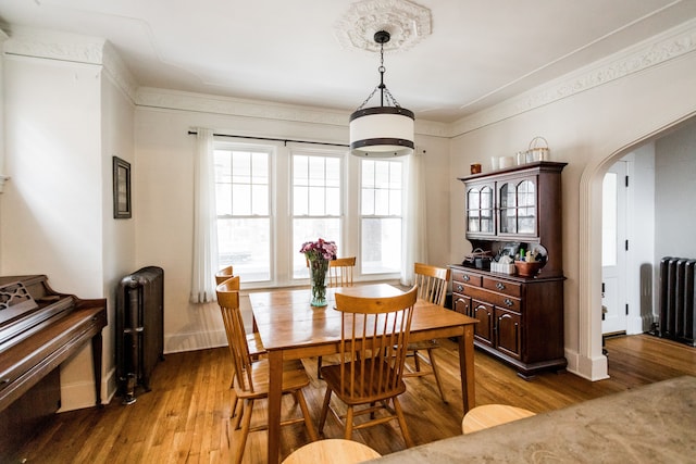 dining area featuring arched walkways, radiator, baseboards, and wood finished floors