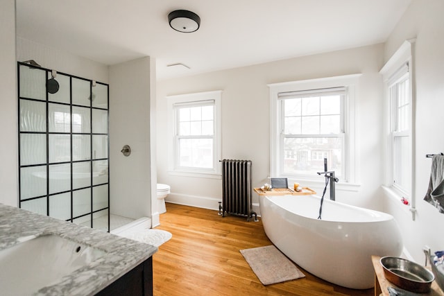 bathroom featuring radiator, wood finished floors, a freestanding bath, a walk in shower, and toilet