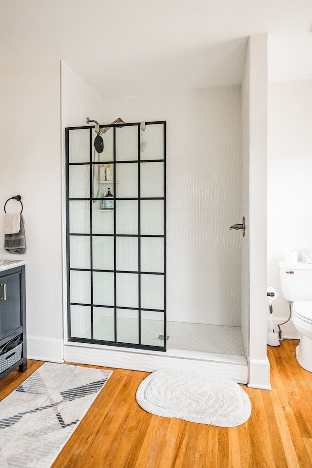 bathroom featuring toilet, wood finished floors, baseboards, and walk in shower